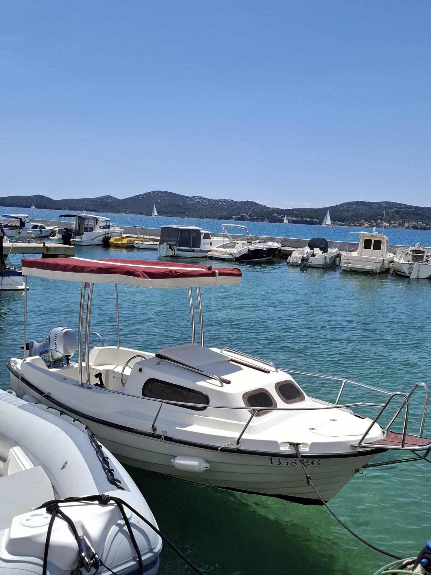 Adria M-Sport 500 family boat with burgundy canopy docked in Biograd harbour